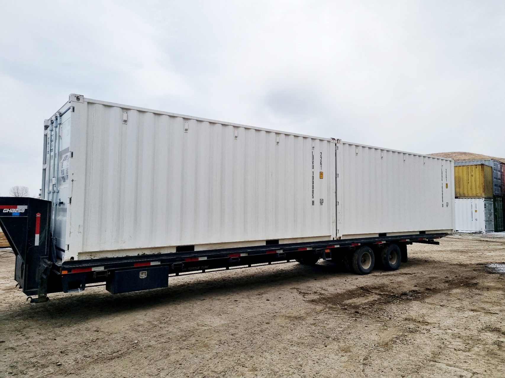 Professional delivery of new or used shipping containers in Alberta being placed on-site via a specialized tilt-bed trailer.